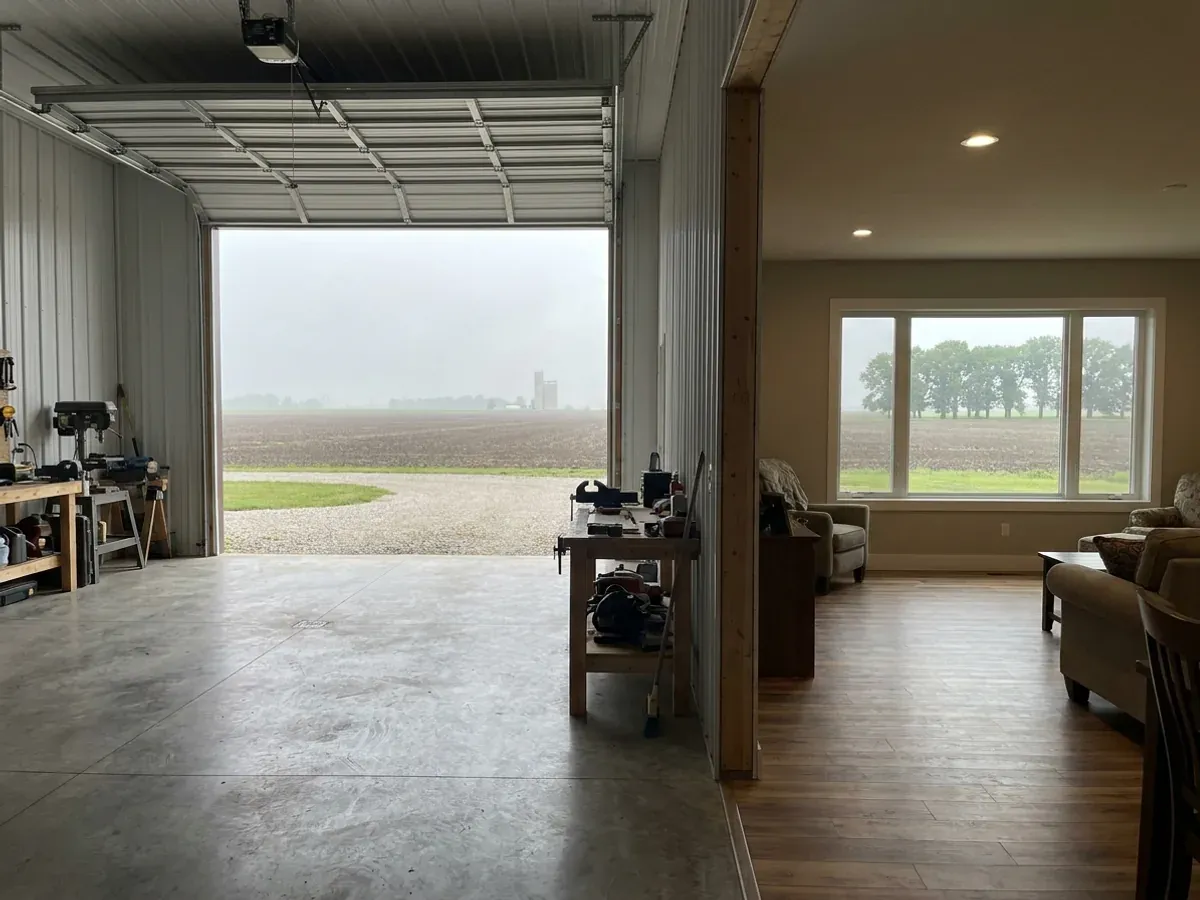 The interior of a shouse where a finished living area with warm flooring meets a shop bay with polished concrete and a tall roll-up door.